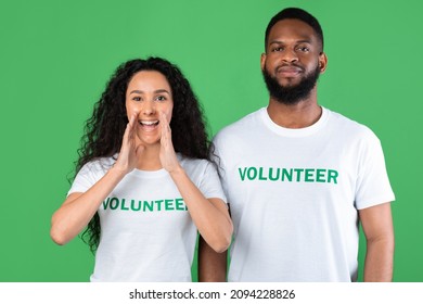 Two Multiethnic Volunteers Shouting Hey Holding Hands Near Mouth  Drawing Attention And Calling You Standing Posing Over Green Background  Volunteering Advertisement  Studio Shot