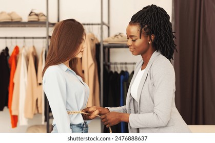 Two multiethnic women explore a selection of clothing items displayed neatly on a rack in a shopping area. Fashion designer measuring client waist - Powered by Shutterstock