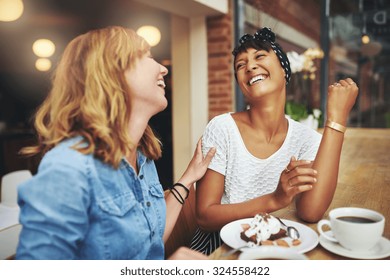 Two Multiethnic Young Female Friends Enjoying Coffee Together In A Restaurant Laughing And Joking While Touching To Display Affection
