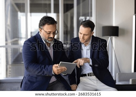 Two multiracial businessmen using tablet, brainstorm ideas for online project, checking financial forecasts, evaluating team performance data, planning company strategy, collaborating on business plan