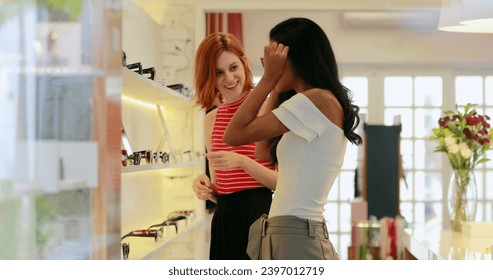 Two multiracial friends shopping for sunglasses, woman looking at mirror for sunwear product