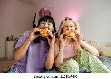 Two multiracial girls in eye patches eating burgers together at home - Powered by Shutterstock