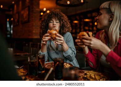 Two multiracial happy friends eating burgers and enjoying a time together in a pub