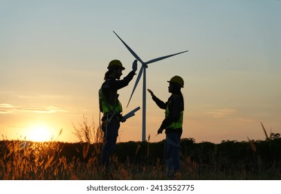 Two multiracial industrial workers examining wind turbines blueprints with amazing sunset on background. Rural area with eco farm of production clean green energy. - Powered by Shutterstock