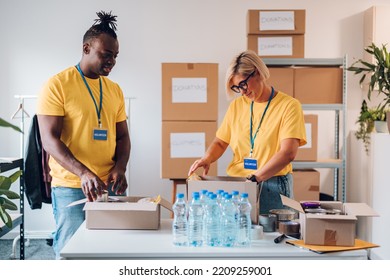 Two Multiracial People Working On Humanitarian Aid Project. Teamwork In Homeless Shelter. Diverse Couple Of Volunteers Working In A Community Charity Donation Center. Copy Space..