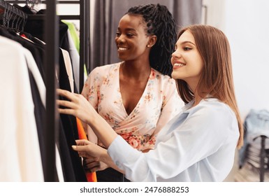 Two multiracial women examining various clothes on a rack in a bustling department store, both engrossed in their selections. - Powered by Shutterstock