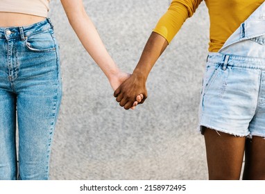 Two multiracial women holding hands - Young adult lesbian couple standing together outdoors - Powered by Shutterstock