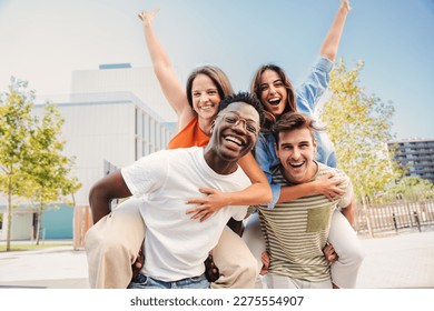 Two multiracial young friends giving piggybacks ride to his girlfriends. A group of happy people having fun and smiling at weekend activity. Men carrying women on his shoulders looking at camera. High - Powered by Shutterstock