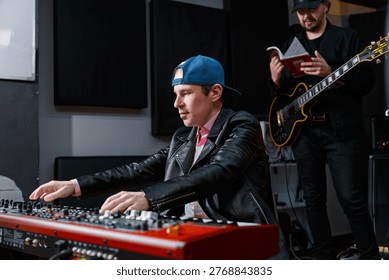 Two musicians are engaged in a studio session, interacting with a keyboard and a guitar. The scene reflects creativity and collaboration in an artistic and professional environment.