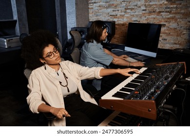 Two musicians are sitting in a recording studio, working together at a keyboard, rehearsing for their music band performance. - Powered by Shutterstock