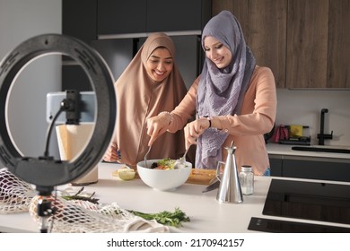 Two Muslim Food Vloggers Smiling While Tossing A Salad At Modern Kitchen.