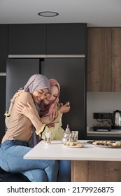 Two Muslim Friends Hugging, Drinking Tea And Eating Arabic Sweets At The Kitchen Table.