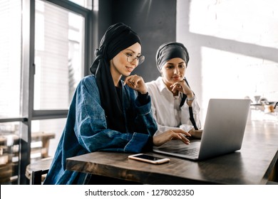 Two Muslim girlfriends in hijabs are doing online shopping for a laptop in a cafe - Powered by Shutterstock