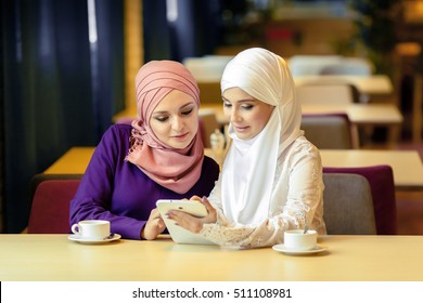 Two Muslim women in a cafe, shop online using electronic tablet