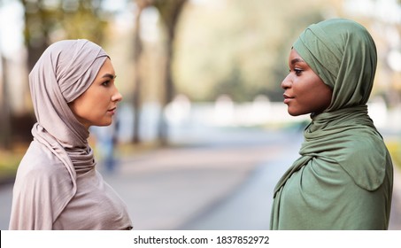 Two Muslim Women Enemies Standing Separately Looking At Each Other With Cool Attitude Posing In Park Outdoors. Fake Female Friendship, Snobbery Concept. Side View Portrait