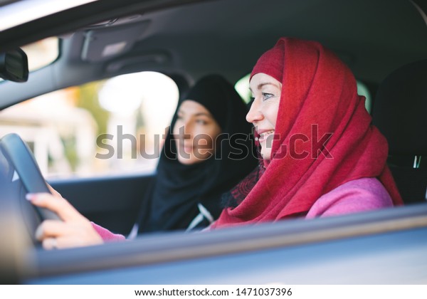 Two muslim women inside\
a car - mother and daughter traveling together - islamic women only\
taxi driver