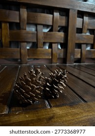 Two natural pine cones placed on a dark wooden table with a soft blurred bokeh background, cozy atmosphere.