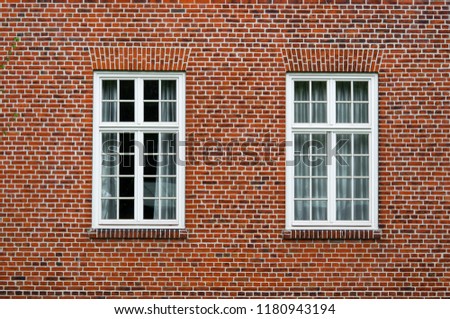 Two neighboring windows with white frames in a urban red bricks clinker house.