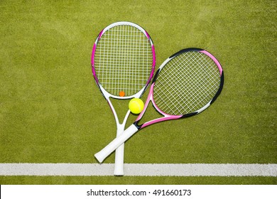 Two new pink tennis rackets with a tennis ball on a green grass court outdoors in summer or spring