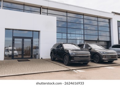 Two new suv parked in front of a modern car dealership building with large windows reflecting the sky