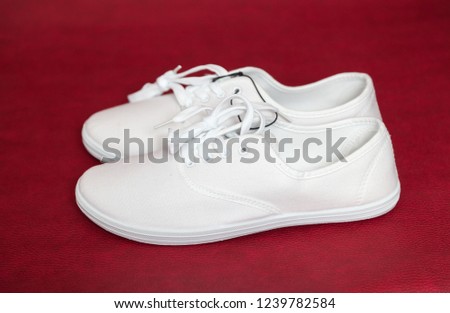 Two new white sneakers with laces stand on a red isolated background.
