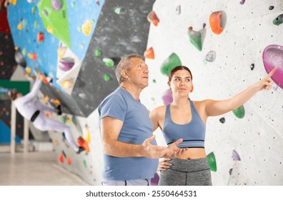 Two novice climbers, young girl and elderly man, standing in training room against backdrop of artificial bouldering wall, discussing with interest routes and techniques of climbing. - Powered by Shutterstock