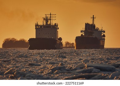 Two nuclear-powered icebreakers are on the frozen sea among the ice floes against the backdrop of a bright sunset sky in winter, close-up. Northern Sea Route in the Arctic