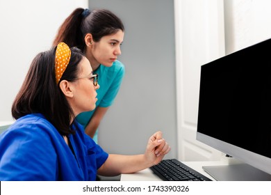 Two Nurses Using A Computer In A X-ray Room, One Of Them Wearing Glasses And Sitting Near The Desk