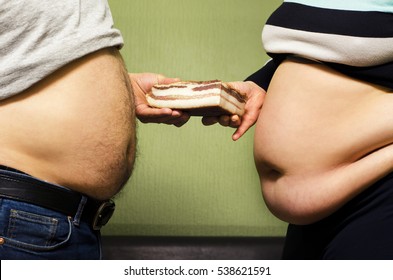 Two obese people (man and woman/ husband and wife) showing big stomachs and holding bacon between them , unhealthy eating concept 
