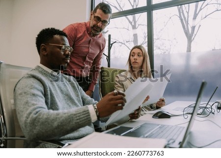 Two office employees reading the documents and typing on their laptops while their boss oversees everything
