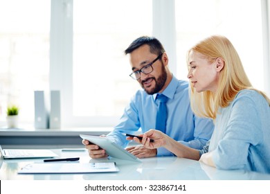 Two Office Workers Discussing Data In Touchpad At Meeting