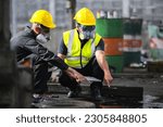 Two officers wearing gas masks inspected the area of a chemical leak in an industrial warehouse to assess the damage. Technicians wearing gas masks inspect and assess the recovery of toxic spills.