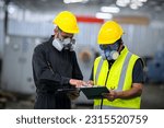 Two officers wearing gas masks, holding tablet and book, inspect the chemical spill site in an industrial warehouse to assess the damage, wearing gas masks, inspecting and evaluating toxicity of leak.