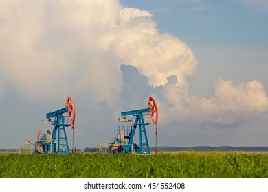 Two oil pump industrial in green field on cloudy sky background