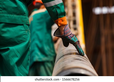 Two Oil Workers In Green And Orange Work Wear And Work Gloves With Rusted Drilling Pipe. Close Up Of One Worker's Hand. Low Depth-of-field. Oil Deposit In Kazakhstan