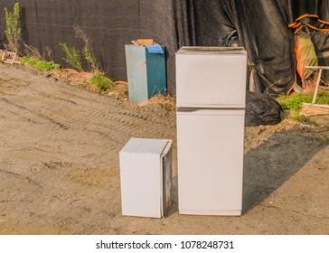 Two old abandoned refrigerators sitting in front of structure covered with black mess material. 