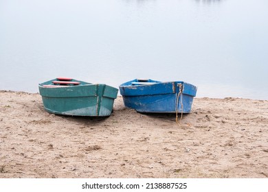 Two old boats on the sandy shore. Two small wooden boats on the sand near the pond.