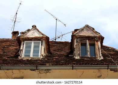 Two Old Destroyed Roof Windows With Cracked Wooden Frames On Top Of Ruins Of Abandoned Suburban Family House Surrounded With TV Antennas And Broken Roof Tiles On Grey Sky Background