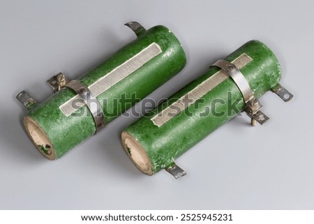 Two old high-power wirewound adjustable resistors on a ceramic core protected with green enamel coating and three tapping points on a gray surface