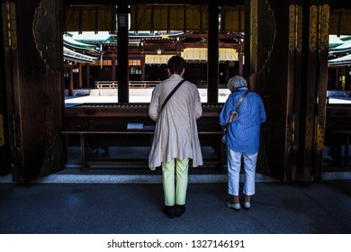 Two Old Japanese Women Praying At The Famous Meiji Shrine In Tokyo, Japan. Old Asian Ladies Offer Prayers At The Biggest Shinto Shrine Of Tokyo City. People Who Worship At Meiji Jingu Temple.