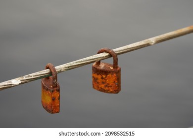 Two Old Love Padlock Left On Bridge Wire. Superstition To Commemorate Their Indestructible Bond And Passion. Water Out Of Focus In The Background. Romantic Act And Urban Legend Concept.