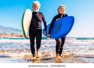 two old and mature people having fun and enjoying their vacations outdoors at the beach wearing wetsuits and holding a surfboard to go surfing in the water with waves - active senior smiling sporting - Powered by Shutterstock