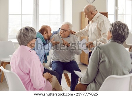 Two old men argue, exchange negative opinions, offend, insult each other while sitting with other senior people at talking therapy session devoted to constructive communication and conflict resolution