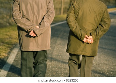 Two Old Men Walking In Park While Holding Their Hands On Back