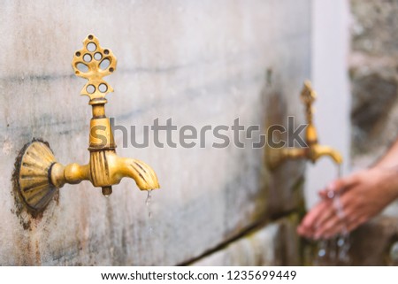 Two old public taps in Istanbul, Turkey. Water flowing and person washing hands in background.
