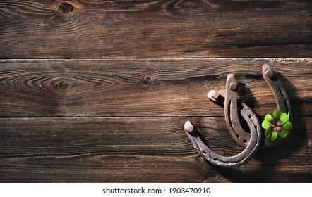 Two old rusty horse shoes and four leaf clover as symbol for lucky charm on a rustic wooden background