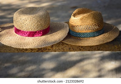Zwei alte Strohhüte, einer für eine Frau und einer für einen Mann, liegen Seite an Seite auf einer Holzbank im Schatten, mit Platz für Text darunter