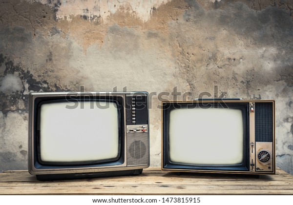 Two old television\
on wood table with old concrete wall background. Vintage TV filter\
tone. Retro style 