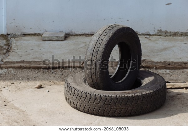 Two old tires from car lie on road discarded against\
background of wall