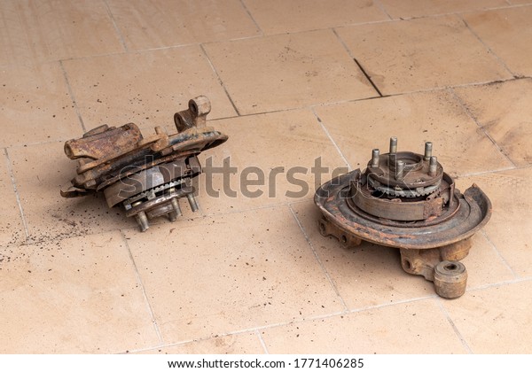 Two old, used, rusty rear hubs, on\
which the brake pads of the parking brake are visible, without\
brake disc on the beige tiled floor of the car repair\
shop